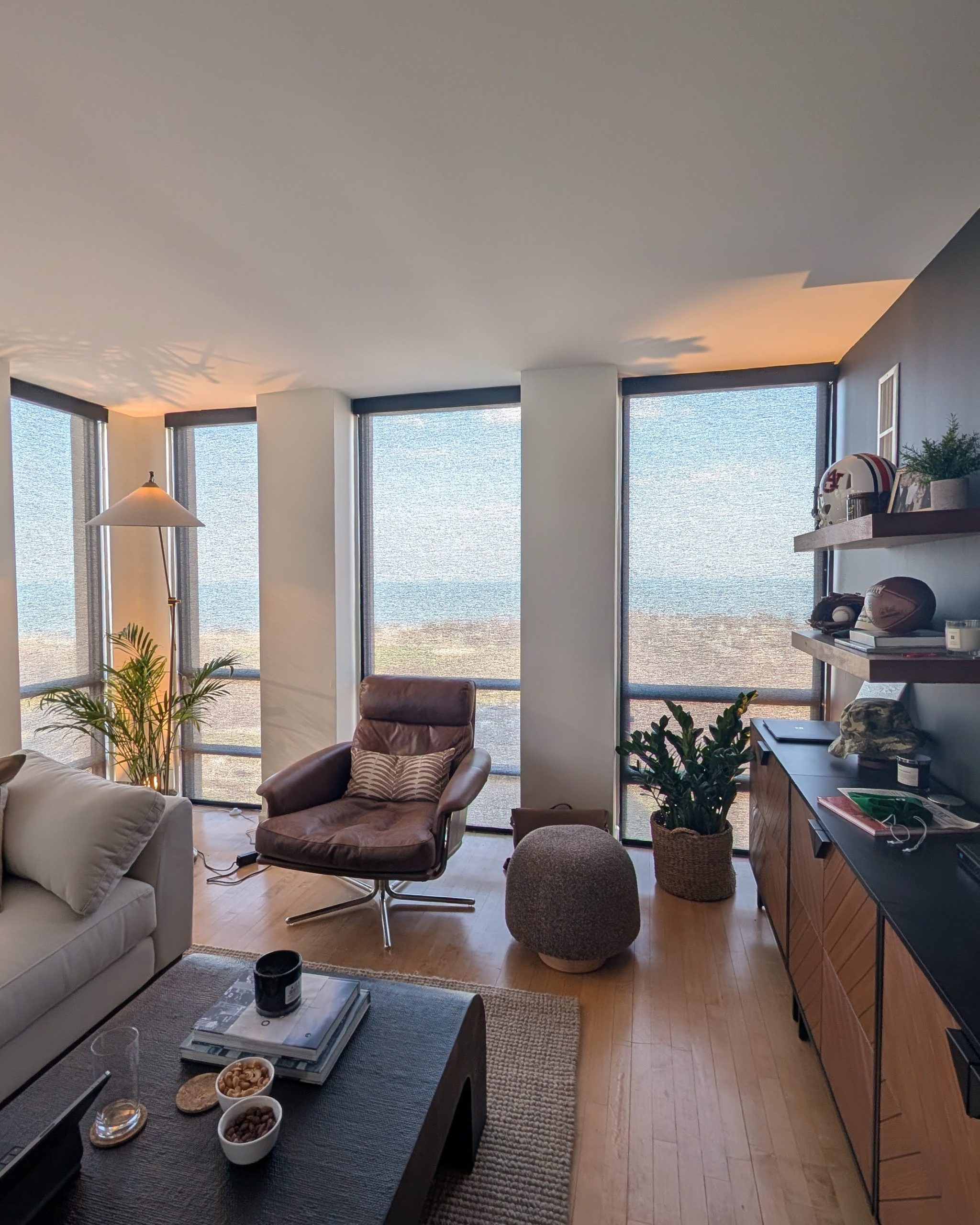 Bright living room with large windows offering a beach and ocean view, a brown leather chair, gray sofa, and a dark coffee table.
